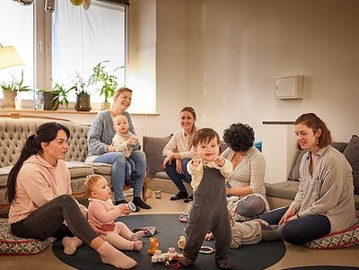 Eine Gruppe Mütter mit Kleinkindern sitzt fröhlich im Spielbereich des ANNA.
