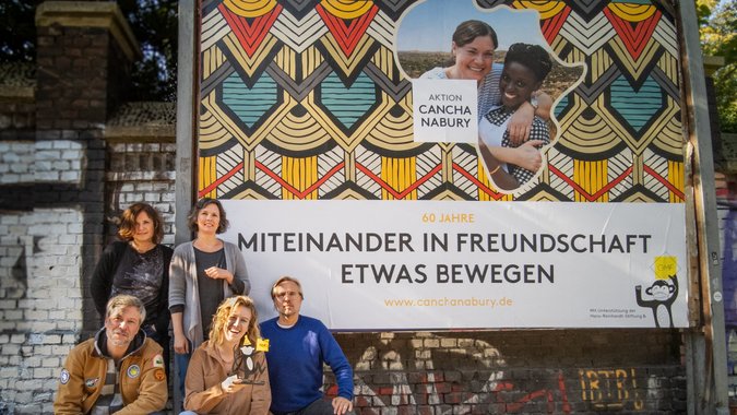 Team GMF und Aktion Canchanabury vor Plakat Kampgane zum 60. Jubiläum